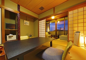 A traditional Japanese-style room with tatami flooring, a low table, a sofa, and sliding doors leading to a balcony. - Daikans (Chikushino)