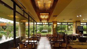 A spacious indoor area with tables and chairs, large windows offering views of a garden, and a modern chandelier. - Daikans (Chikushino)