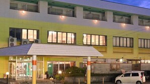 Un hotel con fachada verde y blanca, múltiples ventanas y una entrada visible con porche cubierto.