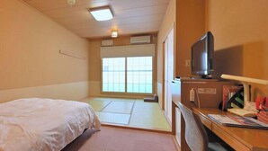 Habitación de hotel con cama, escritorio con televisor y ventana con vistas al exterior.