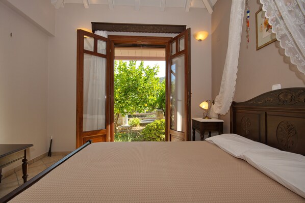 A bedroom with a bed, a bedside table, a lamp, and an open door leading to a garden.