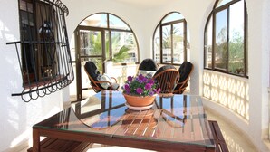 A glass-top table with a potted plant, surrounded by wicker chairs, in a sunlit room with arched windows. - CASA CARLOS - Private Villa Detached with Pool (Cdad. Quesada)