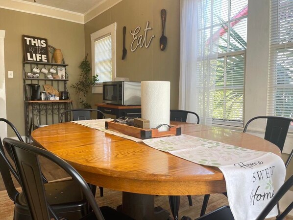 A dining area with a wooden table, chairs, a TV, and kitchen appliances. - Vidalia Sweet Onion Home in Downtown Lyons, with King Bed-Travel Workers Welcome (Lyons)
