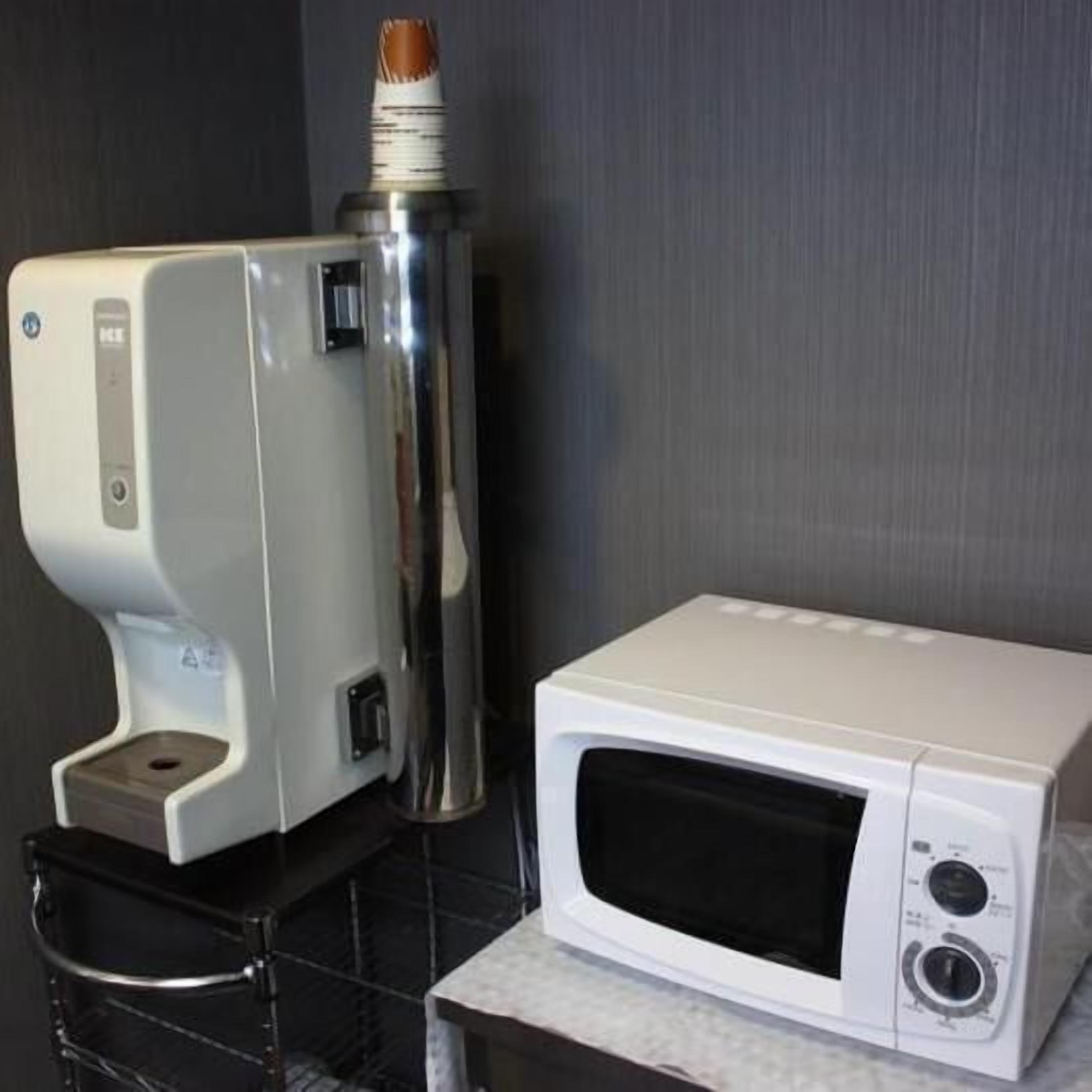 Un horno microondas blanco sobre una encimera junto a un dispensador de gel hidroalcohólico.