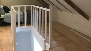 A room with exposed wooden beams, a white staircase, and a bed with a green blanket.