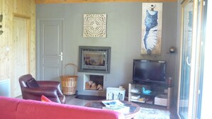 A living room with a fireplace, television, and a large painting on the wall. - Chalet on the shore of Lake Séchemailles (Ambrugeat)