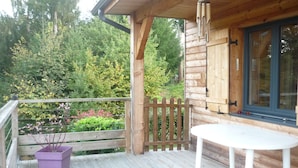 A wooden deck with a white table and a purple planter. - Chalet on the shore of Lake Séchemailles (Ambrugeat)