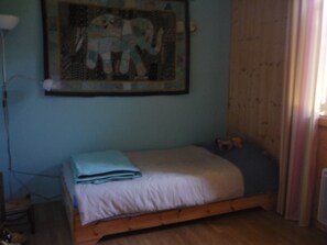 Un dormitorio con una cama individual, un cuadro colgado en la pared y una ventana con cortinas.