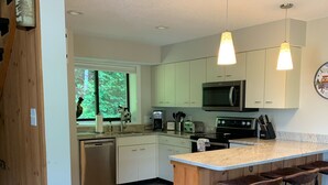 A modern kitchen with wooden cabinets, a central island with bar stools, a built-in microwave, and a large window offering a view of greenery. - Sun Soaked Views, Pool, Spa; and Spectacular Mountain Views (Lincoln)