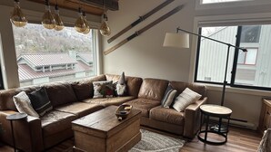 A cozy living room with a sectional sofa, a wooden coffee table, and a large window with a view of buildings. - Sun Soaked Views, Pool, Spa; and Spectacular Mountain Views (Lincoln)