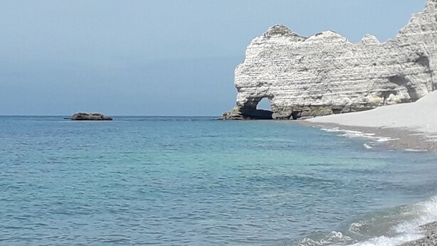 A coastal scene with clear blue water, a sandy beach, and white rock formations.