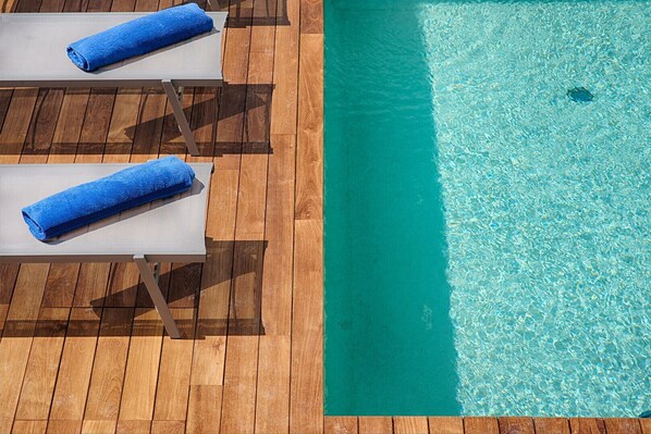 Un espace aménagé au bord de la piscine, avec deux chaises longues et une terrasse en bois.