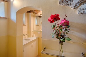 Une salle de bain avec un lavabo, un miroir et un vase de fleurs.