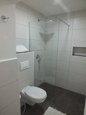 A modern bathroom with a shower, toilet, and a small shelf. - Penthouse Apartment Sveti Stefan (Sveti Stefan)