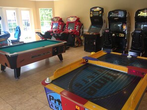 Mesa de bilhar, jogos de fliperama e mesa de sinuca em área de lazer.