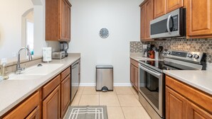 A modern kitchen with wooden cabinets, stainless steel appliances, a microwave, and a clock on the wall. - Modern Vista Cay nr pool•Walk to OCCC close iDrive (Orlando)