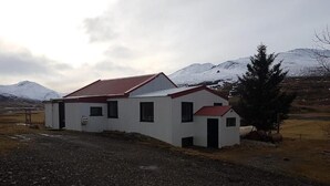 Ein weißes Gebäude mit rotem Dach, gelegen in ländlicher Umgebung mit einem Berg im Hintergrund.