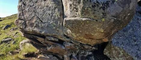 A large rock formation with a rugged texture and moss growth, surrounded by smaller rocks and sparse grass.
