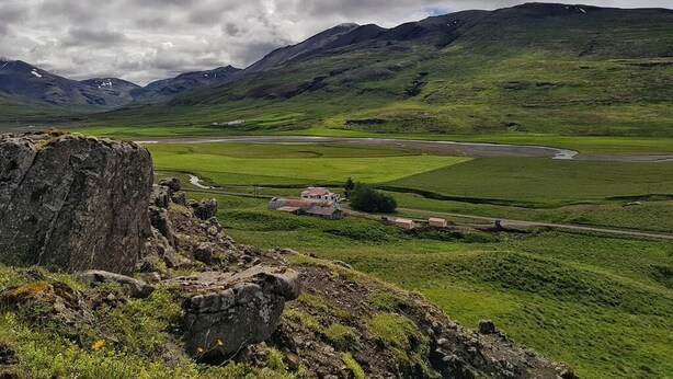 Eine gebirgige Landschaft mit einer kurvenreichen Straße, einer kleinen Siedlung und einer großen Felsformation.