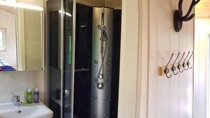 Ein modernes Badezimmer mit einer gläsernen Duschkabine, einem Waschbecken mit Pflegeprodukten und einem Wandpaneel zur Aufbewahrung.