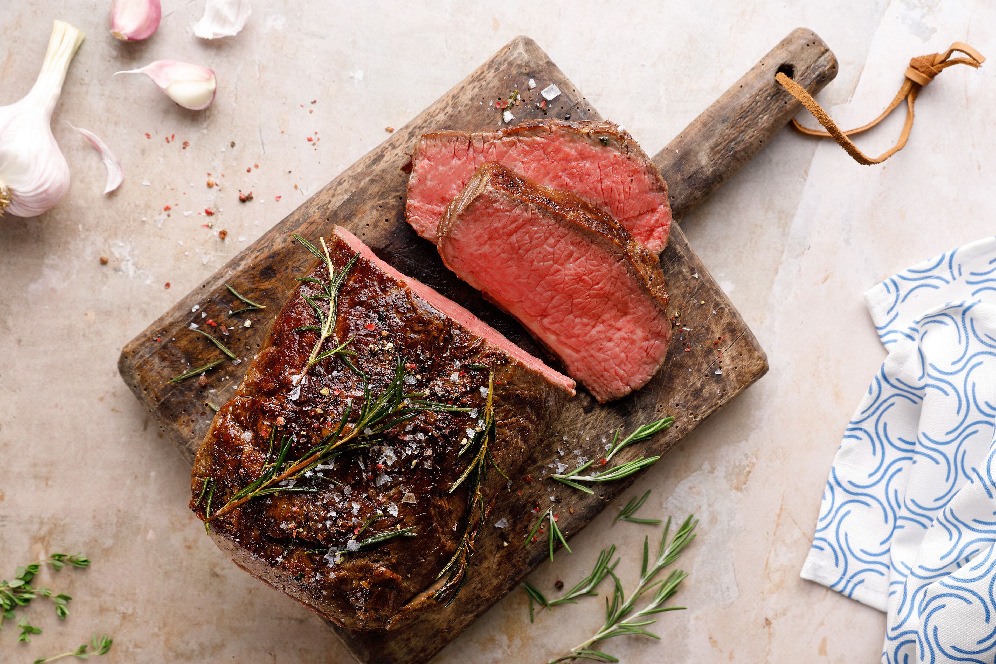 A steak with rosemary and salt on a wooden board.