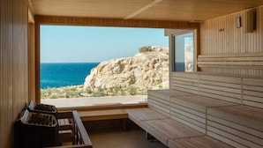 A wooden interior with a bench and a window overlooking a rocky coastline. - ROBINSON IERAPETRA (Ierapetra)