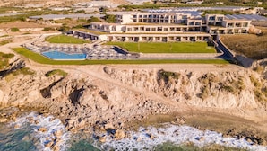 Vista aérea de un hotel costero con varias edificaciones, piscina y costa rocosa.
