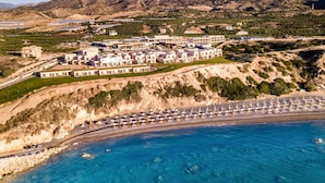 A coastal resort with multiple buildings, a beach with umbrellas, and mountains in the background. - ROBINSON IERAPETRA (Ierapetra)