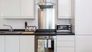 A modern kitchen with white cabinets, a stainless steel range hood, a toaster, a microwave, and a dishwasher. - Belfry Quarters (Redhill)