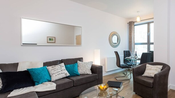 A modern living room with a sofa, armchairs, a glass coffee table, and a dining area with a table and chairs. - Belfry Quarters (Redhill)