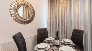 A dining area with a table set for four, a decorative mirror, and a curtain. - Belfry Quarters (Redhill)