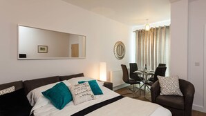 A hotel room with a bed, a dining table with chairs, a mirror, and a door. - Belfry Quarters (Redhill)