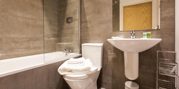 A modern bathroom with a bathtub, toilet, and sink. - Belfry Quarters (Redhill)