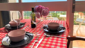 A dining table set with pink bowls, wine glasses, and cutlery, overlooking a scenic view with a colorful umbrella. - Rustic house on montain with privileged views of Mediterranean sea (Pineda de Mar)