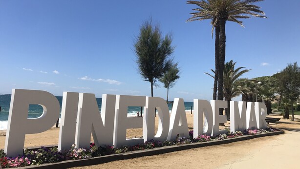 A large sign with the text "PINEDA DEW" surrounded by a flower bed, with a beach and palm trees in the background. - Rustic house on montain with privileged views of Mediterranean sea (Pineda de Mar)