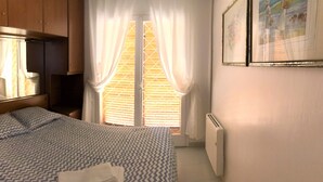 A bedroom with a bed, a mirror, a radiator, and a window with curtains. - Rustic house on montain with privileged views of Mediterranean sea (Pineda de Mar)