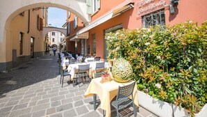 A restaurant with outdoor seating, a large decorative vase, and a stone-paved street. - Villa Barbara (Desenzano del Garda)