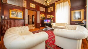 A spacious living room with a large red patterned rug, white leather sofas, a television, and framed artwork on the walls. - Villa Barbara (Desenzano del Garda)