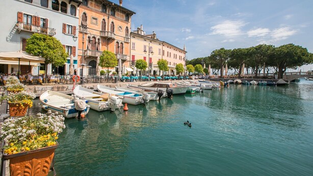 A waterfront area with boats docked, buildings with balconies, and outdoor seating areas. - Villa Barbara (Desenzano del Garda)