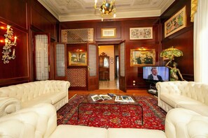 A room with a red patterned rug, two white leather sofas, a television, and framed artwork on the walls.
