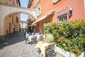Ett utomhuskafé med bord och stolar, en stor ananas som mittpunkt på bordet och en byggnad med en skylt som visar texten ”Ristorante”.