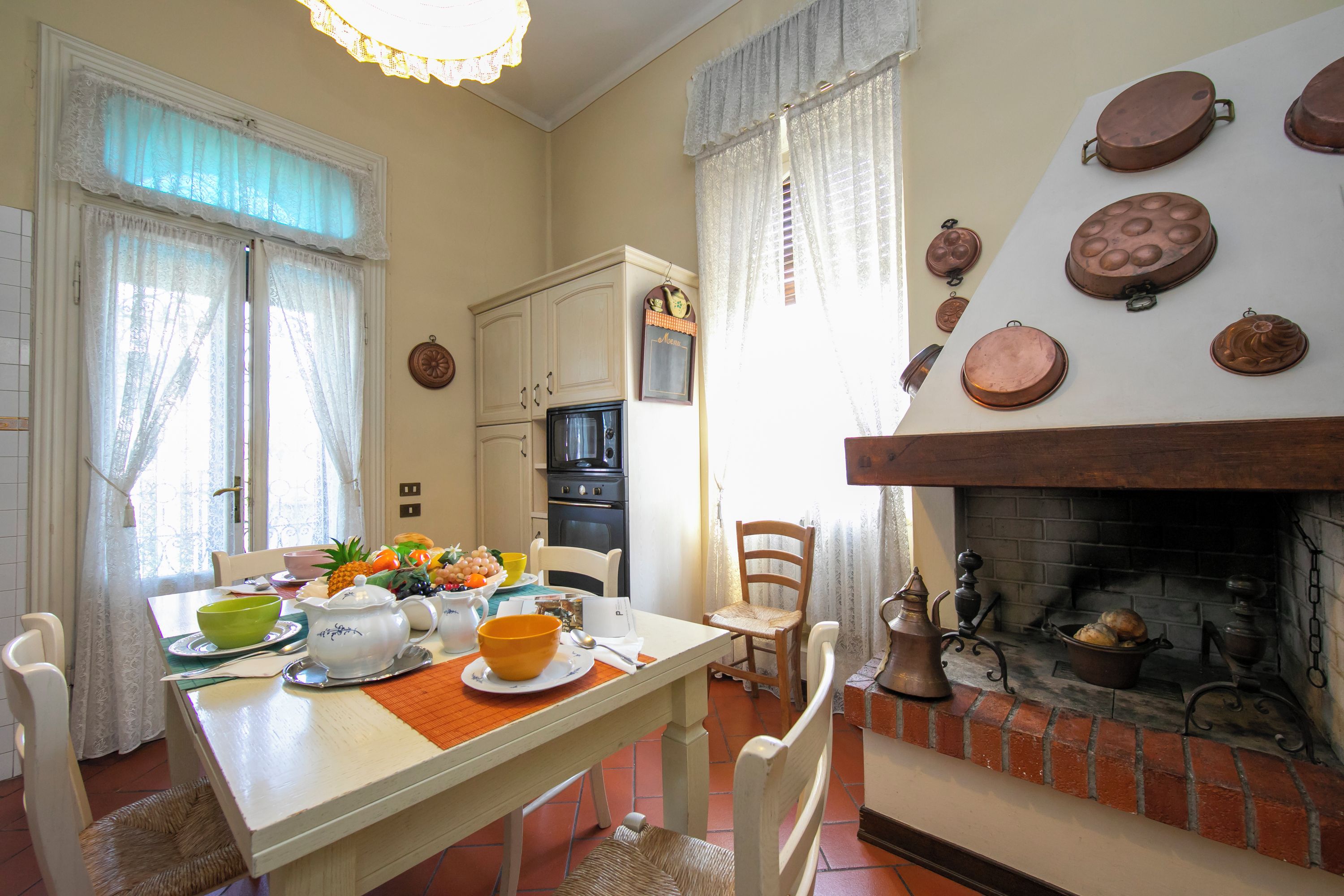 Un'area pranzo con un tavolo apparecchiato per due, un caminetto decorato con piatti e una cucina con mobili ed elettrodomestici.