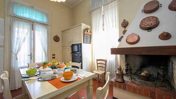 Un'area pranzo con un tavolo apparecchiato per due, un caminetto decorato con piatti e una cucina con mobili ed elettrodomestici.