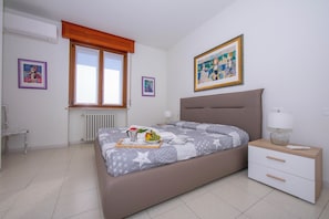 Een slaapkamer met een bed, nachtkastje, lamp en kunstwerken aan de muren.