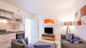 A modern kitchen with a microwave, stove, and oven, a living area with a sofa and TV, and a door leading to another room. - Casa dei Quadri (Peschiera del Garda)