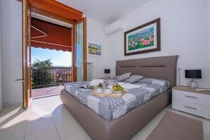 Une chambre à coucher comprenant un lit, des tables de chevet, une commode, une fenêtre avec vue et un balcon.