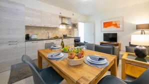 A modern kitchen with white cabinets, a dining table set with plates, a basket of bread, and a TV in the background. - Casa dei Quadri (Peschiera del Garda)
