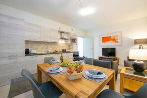 A modern kitchen with white cabinets, a dining table with chairs, a TV, and a lamp.