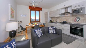 A modern kitchen with a dining area, a sofa with decorative pillows, and a ceiling fan. - Casa dei Quadri (Peschiera del Garda)