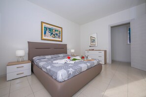Une chambre moderne avec un grand lit, des tables de chevet, une commode, une coiffeuse et un tableau encadré au mur.